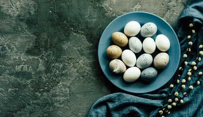 Blue plate with Easter eggs and a feather on a concrete background. Top view with copy space.