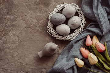 Easter eggs in nest on grey background. Easter background with eggs and spring flowers. Top view with copy space.