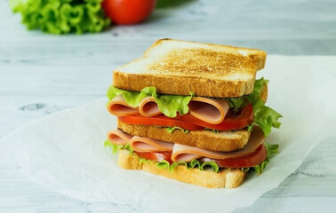 cold cut turkey sandwich on whole wheat with ham, lettuce, tomato on wooden background