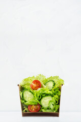 Wellness take away appetizer - fresh healthy salad of raw vegetables in craft package for fast food with showing ingredients inside on soft light white background, vertical.