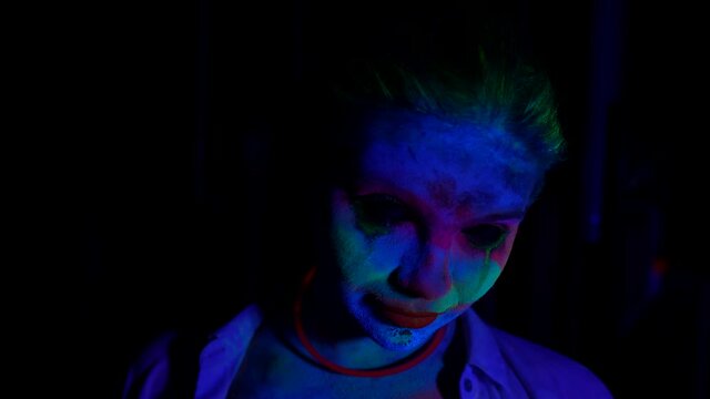 horror movie concept, portrait of woman with flourescent paints on face in darkness