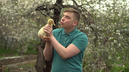 A young man holds a real duckling in his arms. A man in the garden with a bird.