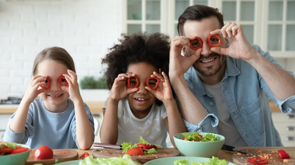 Family portrait of happy young Caucasian father and little multiethnic daughters make glasses with...