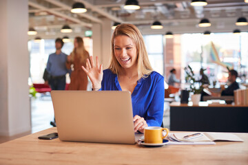 Young Businesswoman Sitting At Desk On Video Call In Modern Open Plan Office