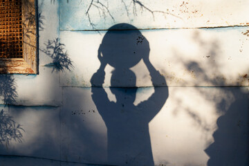 The shadow of a teenage boy holds a large round ball over his head