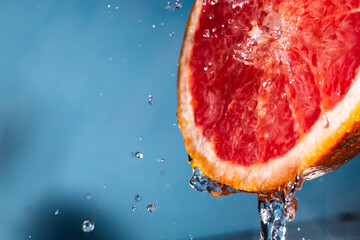 water drips from half a grapefruit. Splashes and drops fly from a piece of grapefruit symbolizing the brightness and freshness of its taste