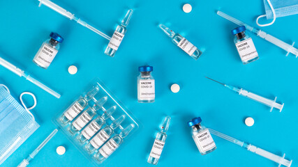 Covid vaccination concept. Coronavirus Covid-19 vaccine vials, ampoules, syringes, protective face masks, pills on a blue medical background. Top view. 