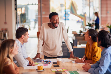 Businessman Giving Presentation To Colleagues Sitting Around Table In Modern Open Plan Office