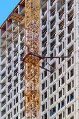 Close up view of frame part of metallic crane machinery attachment at windows of new residential building construction site. Windows with sky reflection.
