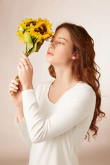 Young red-haired lady in white long sleeve t-shirt is looking at the bunch of yellow sunflowers. Romantic lady is holding the graceful bouquet in front of her face. 