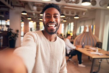 Portrait Of Young Businessman Taking Selfie On Mobile Phone In Modern Open Plan Office