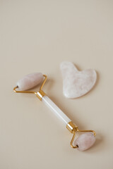 Flatlay of gua sha massage roller and stone scraper tool on neutral beige background. Aesthetic beauty skin care wellness treatment concept