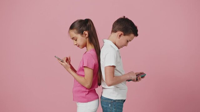 Little brother and sister networking online on smartphones, ignoring real communication, standing back to back