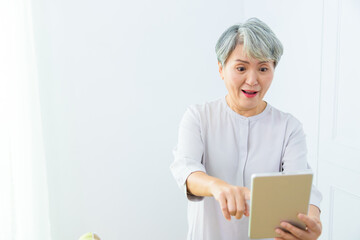 Smiling middle-aged Asia woman browsing wireless Internet on tablet at home, happy modern senior female using pad device, elderly technology concept.