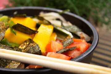 A closeup photo of poke with tomato, slices of mango, chives and seaweed.