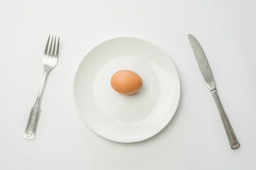 Dish with one raw egg fork and knife isolated on white background.Top view minimal food concept.