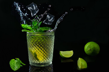 Refreshing mojito cocktail with ices cubes splash with fresh limes and mint on dark background.Studio shot of tropical drink with copy space.