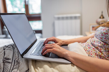 Woman's hands working with laptop tucked in bed