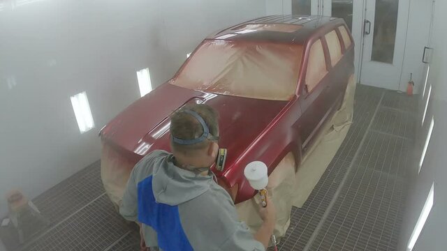 Car colouring process held by the worker. Repairman painting car with a spray gun. Man in uniform painting car
