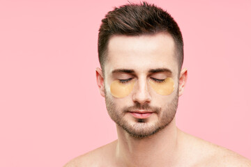 Young handsome man with closed eyes and golden eye patches on pink background