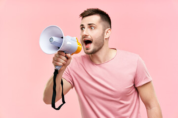Funny young man shouting loud holding a megaphone over pink background