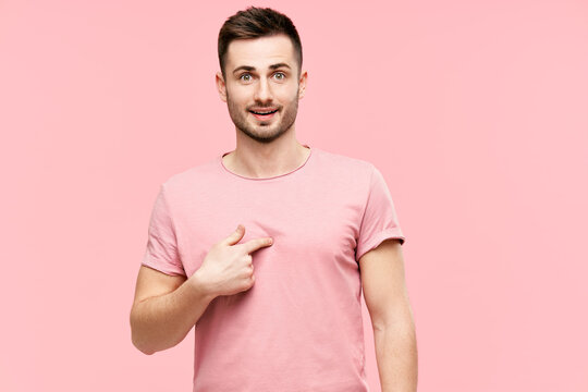 Amazed young man looking surprised pointing himself, making sure he heard righ over pink background
