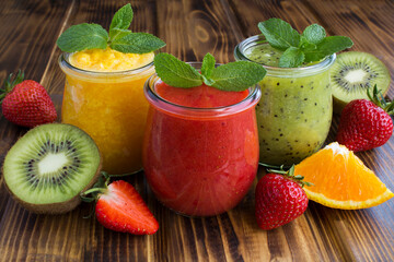 Different fruit smoothie or puree in the small glass jars on the wooden  background. Close-up.