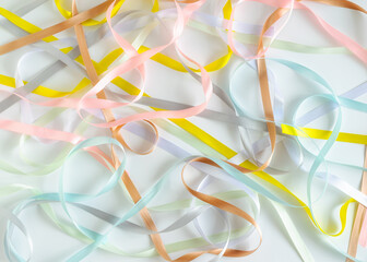 Satin narrow ribbons of pink, white, gray, brown, blue and yellow colors are randomly scattered on a white background. Wallpaper. Horizontal photo. Abstract background. 