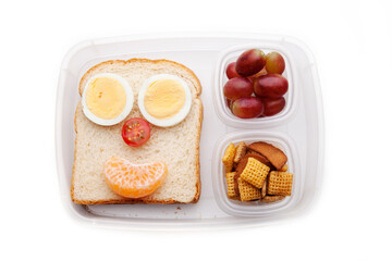 School lunch box snacks for kids over white background. Back to school. Healthy and fun snacks options for parents. Food art creative concepts. Bows with fruits and vegetables and cute face sandwich.