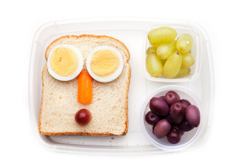 School lunch box snacks for kids over white background. Back to school. Healthy and fun snacks options for parents. Food art creative concepts. Bows with fruits and vegetables and cute face sandwich.