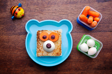 Obraz premium School lunch box snacks for kids over wooden background. Back to school. Healthy and fun snack option for moms. Cute food art creative concepts. Bow with fruits and vegetables and cute sandwich.