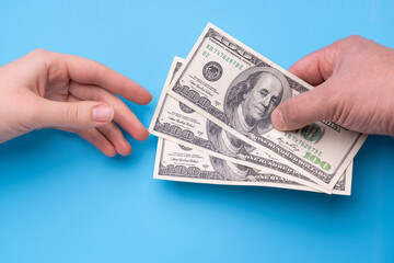 Male hand gives 300 dollars to female hand, blue background - obrazy, fototapety, plakaty