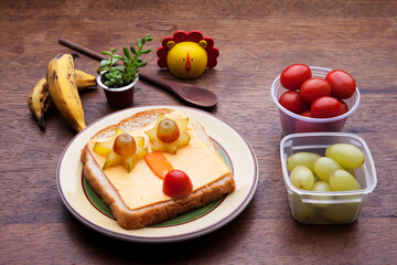 School lunch box snacks for kids over wooden background. Back to school. Healthy and fun snack option for moms. Cute food art creative concepts. Bow with fruits and vegetables and cute sandwich.