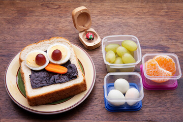 School lunch box snacks for kids over wooden background. Back to school. Healthy and fun snack option for moms. Cute food art creative concepts. Bow with fruits and vegetables and cute sandwich.