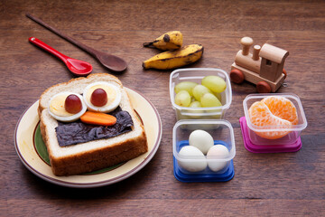 School lunch box snacks for kids over wooden background. Back to school. Healthy and fun snack option for moms. Cute food art creative concepts. Bow with fruits and vegetables and cute sandwich.