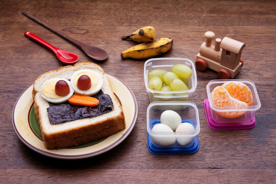 School lunch box snacks for kids over wooden background. Back to school. Healthy and fun snack option for moms. Cute food art creative concepts. Bow with fruits and vegetables and cute sandwich. - Powered by Adobe