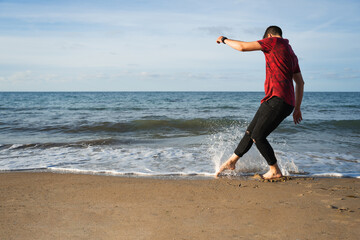 Man on the seashore. He plays with the water with one foot and splashes with the water. Caucasian wearing a short-sleeved T-shirt and long trousers. Unrecognisable, he is on his back.