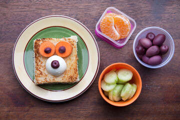 School lunch box snacks for kids over wooden background. Back to school. Healthy and fun snack option for moms. Cute food art creative concepts. Bow with fruits and vegetables and cute sandwich.