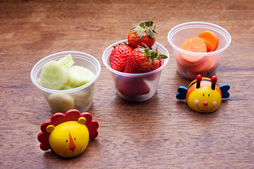 School lunch box snacks for kids over wooden background. Back to school. Healthy and fun snacks options for moms. Cute food art creative concepts. Bows with fruits and vegetables.