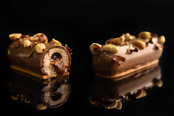 Eclair in glaze with hazelnuts on a black background. Leaking filling from a cut cake..