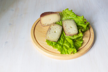 Hard cheese with fenugreek seeds and lettuce leaves on round wooden board on white background