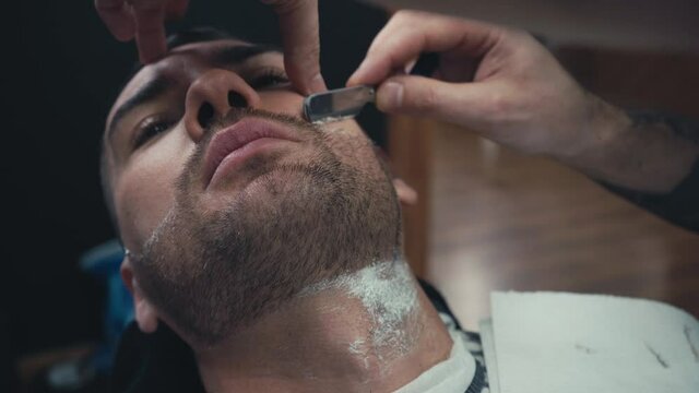 Barber styling beard of client with razor