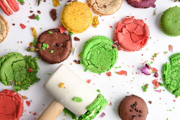 Crushed macaroon of different colors on a white background with a hammer..