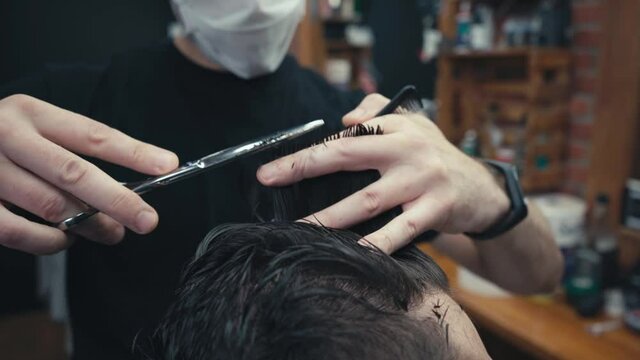 Cropped view of hairstylist cutting hair of client in barbershop