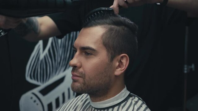 Barber drying and styling hair of client in barbershop