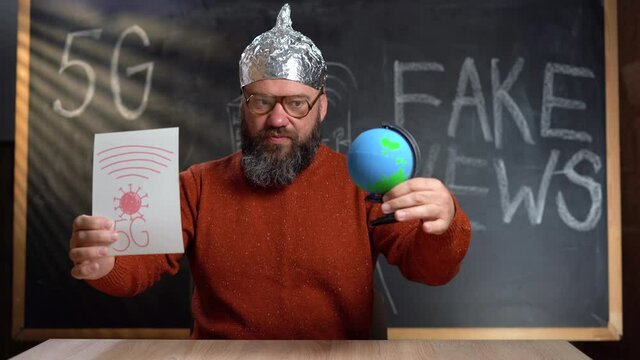 A strange man in a foil hat with a Stop 5G poster. Conspirational fake news. takes off his hat and puts it on the globe. The concept of protection from special services. 4k