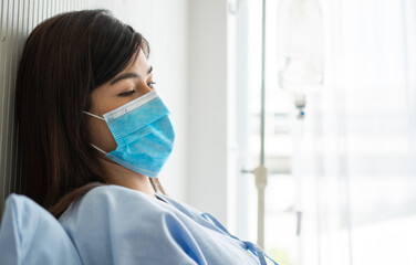 Sad Asian patient woman lying on the hospital bed and wearing a face mask to protect coronavirus. Concept of Health care, quarantine coronavirus (COVID-19), and Health insurance.