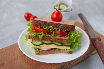 Delicious sandwich with fresh lettuce leaves, tomatoes, cucumbers and cheese on a grey table background.