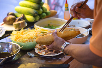 Male hands making Vietnamese sandwich Banh Mi　ベトナムのサンドイッチ バインミーを作る男性の手 - obrazy, fototapety, plakaty