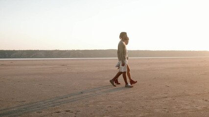 The side view of the African positive couple going to the car on the sand by the hands in the nature